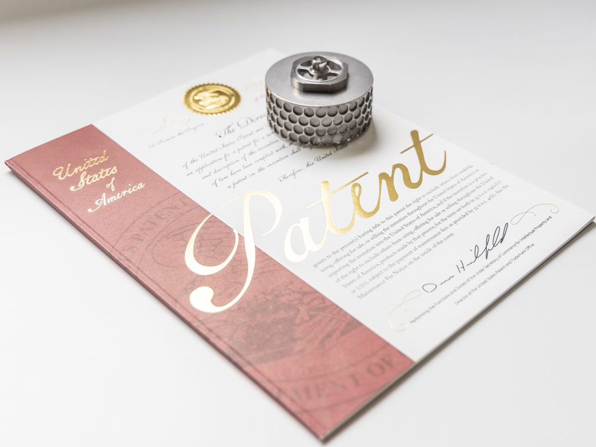 SpinChem rotating bed reactor cylinder with perforated metallic design displayed on a patent document with gold foil embossing.