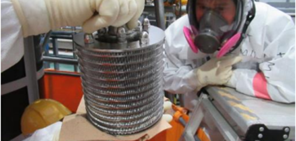 picture of an assembled rotating bed reactor held up between two hands with a person in protective wear and gas mask in the background