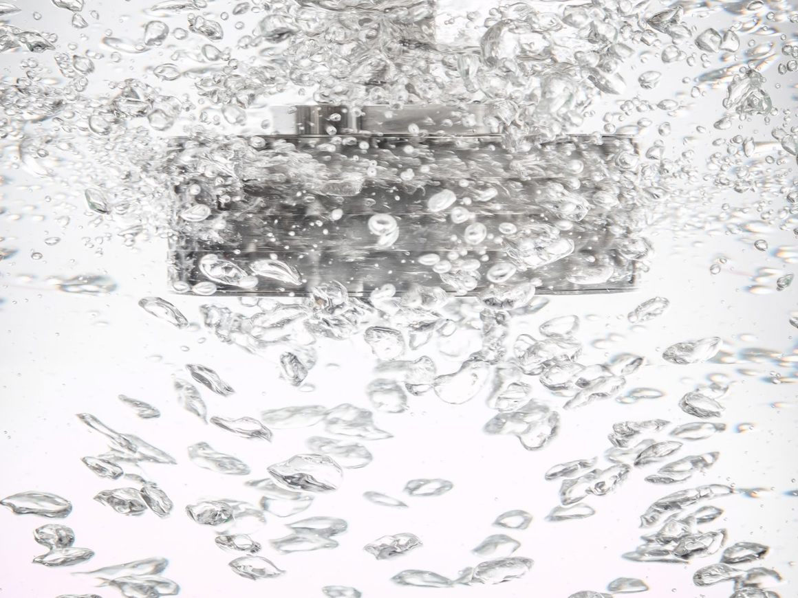 SpinChem rotating bed reactor submerged in water with bubbles and turbulence, showing metallic components visible through clear liquid.